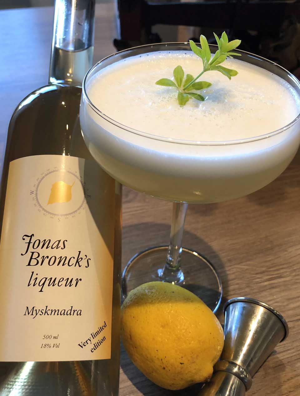 Drink Myskmadra sour & tonic med en flaska liqueur och en citron på ett bord